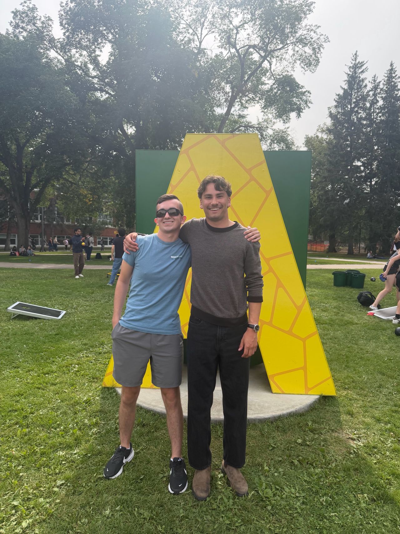 Caden and Michael standing together in front of the green and gold A on the University of Alberta campus.